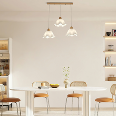 Dreiflammige Pendelleuchte mit weißen Blütenschirmen und Holzdetails elegant über einem langen Esstisch arrangiert